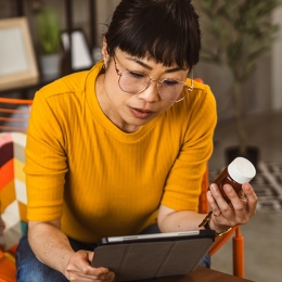Woman in yellow shirt reading a supplement label and reading on an ipad